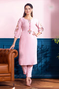 Woman in a pink traditional outfit standing in a room with a blue wall and brown leather chair.