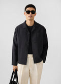 A model wears the Percival black linen overshirt, styled with cream trousers and sunglasses in a studio.