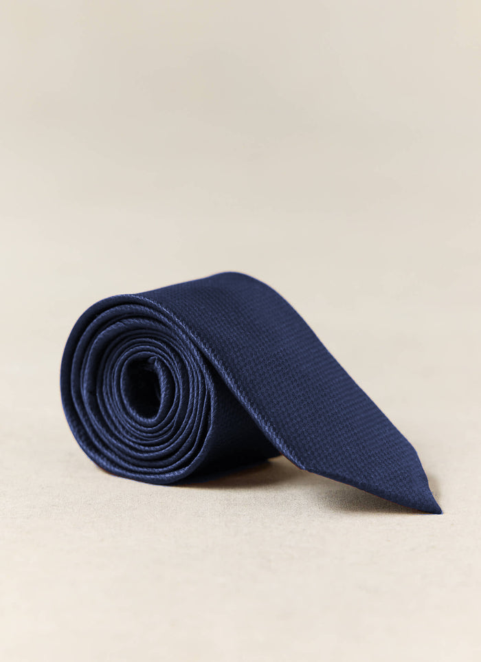 Percival Grenadine Tie | Silk | Navy, rolled to show its textured weave on a neutral studio background.
