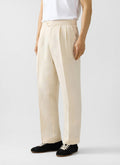 Percival cream linen pleated trousers in a relaxed fit, styled with a white t-shirt and black trainers.