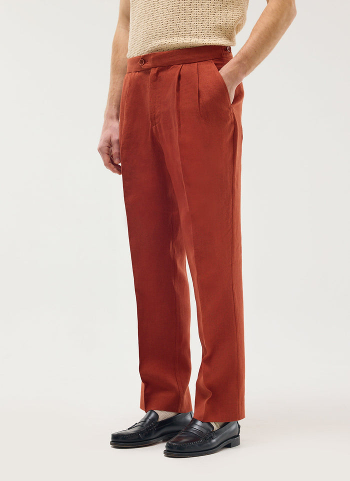 A model wears Percival rust linen pleated tailored trousers with a cream knitted top and black loafers.
