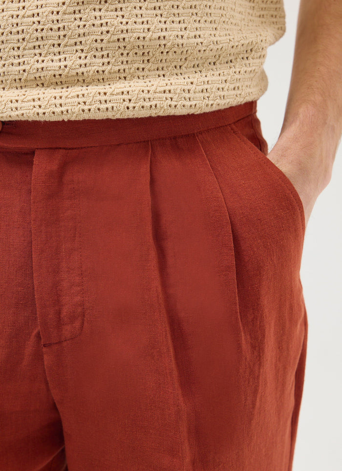 Close up of a model wearing Percival rust linen pleated trousers with a cream knitted top.